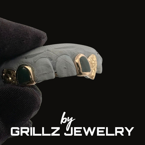 Gray dental grill with gold accents held by a gloved hand, branded 'by Grillz Jewelry'.
