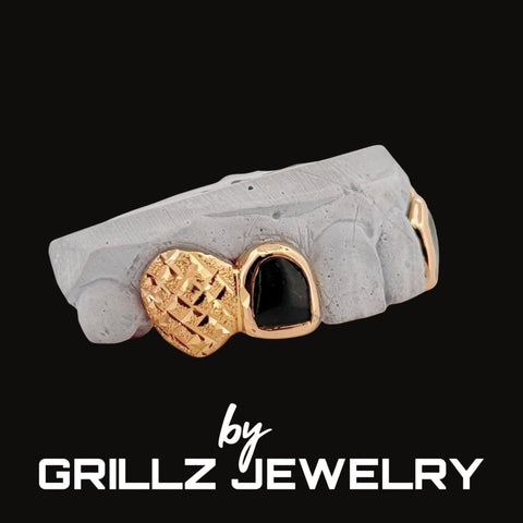 Jewelry piece with gold and black heart design on a gray stone surface, branded by Grillz Jewelry.