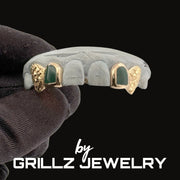 Gray and gold grillz with green stones held by a gloved hand, branded as Grillz Jewelry.