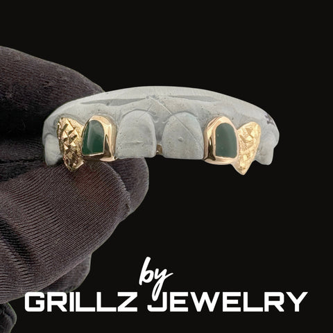 Gray and gold grillz with green stones held by a gloved hand, branded as Grillz Jewelry.