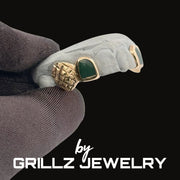 Jewelry with green stone and gold accents on a dark background, featuring 'GRILLZ JEWELRY' branding.