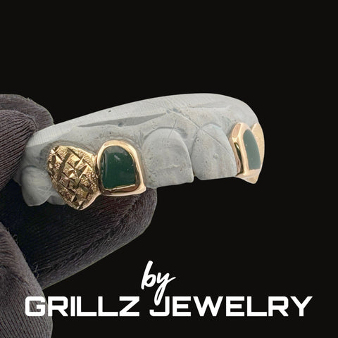 Jewelry piece with gold accents and green stones held by a hand, branded 'Grillz Jewelry'.