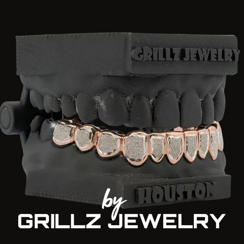 Black grill with rose gold and silver teeth on a black background, branded as Grillz Jewelry.