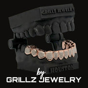 Rose gold grillz on a black mannequin mouth with 'Grillz Jewelry' branding.