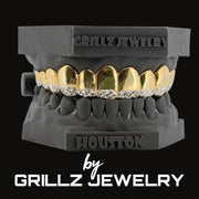 Gold and silver grillz on a black dentures model with 'Grillz Jewelry' branding.