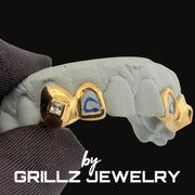 Gold grillz on a mouth mold with 'GRILLZ JEWELRY' branding.