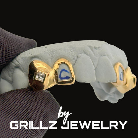 Gold grillz on a mouth mold with 'GRILLZ JEWELRY' branding.